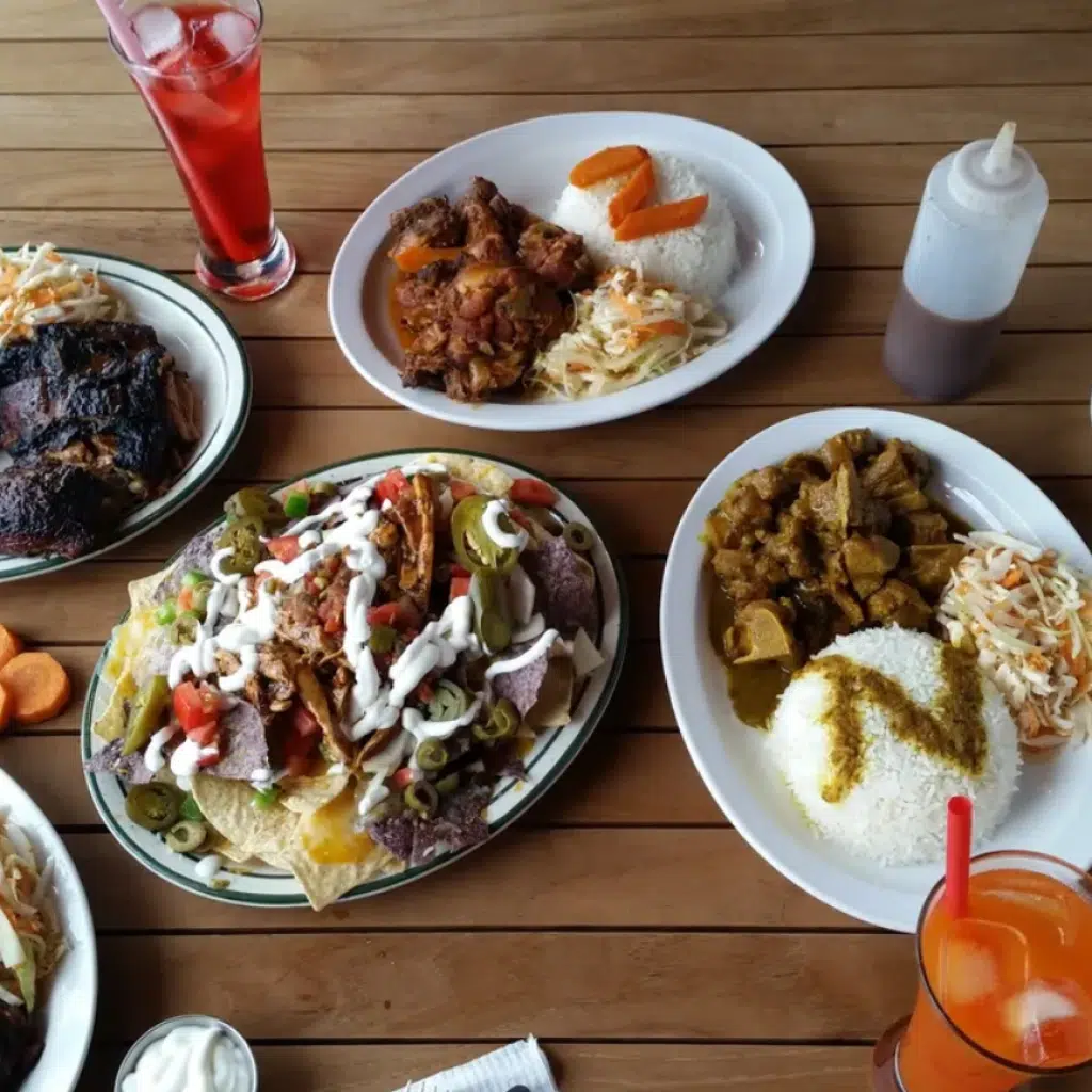 Plusieurs plats y compris des nachos, deux boissons, des plats de viande avec du riz et des sauces sur une table en bois à l'extérieur.