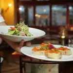 Un serveur apporte deux plats : une salade et un plat de bruschetta.