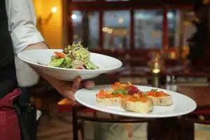 Un serveur apporte deux plats : une salade et un plat de bruschetta.