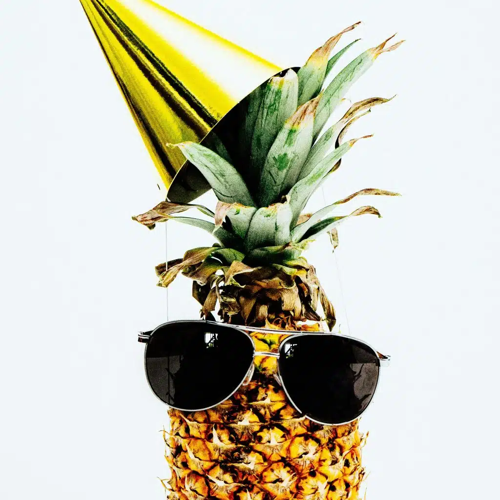 Un ananas portant des lunettes de soleil et un chapeau d'anniversaire doré.